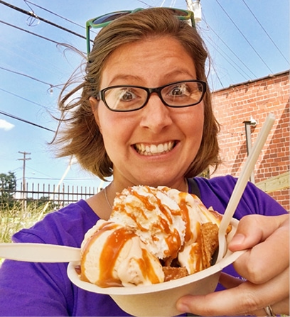 Bethany Planton wears a huge smile as she holds an ice cream sundae drizzled in caramel syrup in front of the camera.