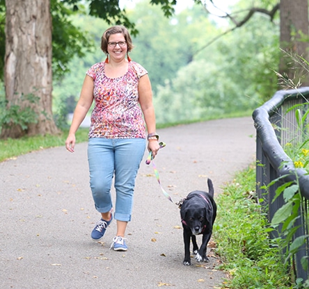 Bethany Planton walks her black dog on a leash down a paved pathway in a park.
