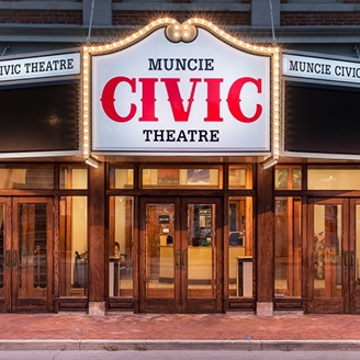 Exterior of a classic style theater building with a brightly lit marquee that reads Muncie Civic Theatre.